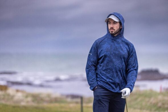 Golfer wearing the PING Saul hooded fleece in Deep Sea Blue Camo on a coastal course.
